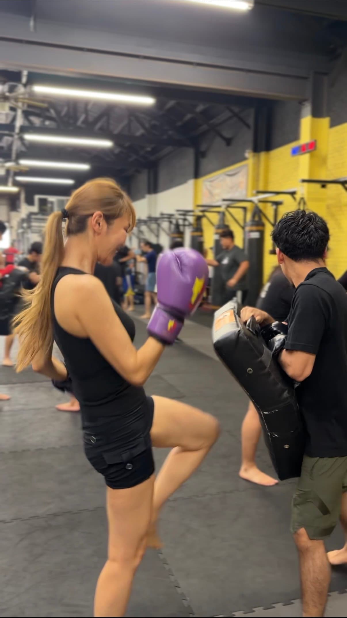 Member throwing a knee strike on Thai pads during a kickboxing class at TAEJO Kickboxing